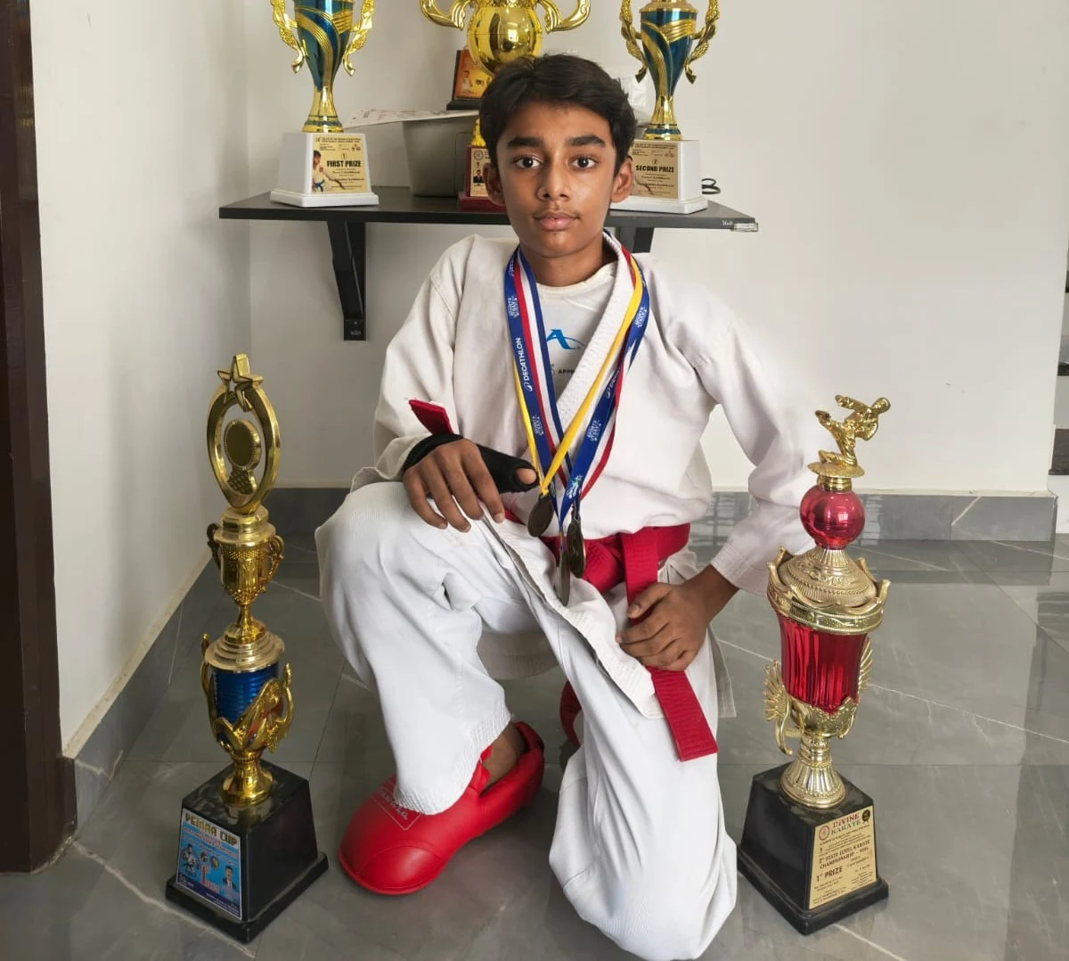Karate student kneeling with medals and trophies