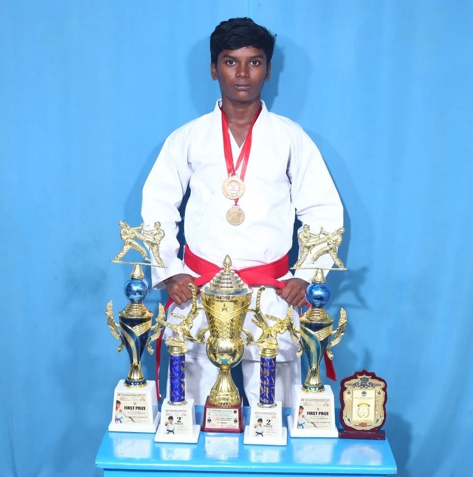 Karate student standing with medals and trophies against a blue backdrop